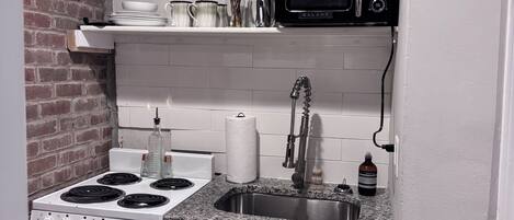 A compact kitchen with a stove, sink, microwave, and white cabinets.