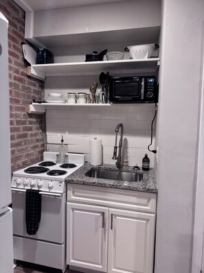 A compact kitchen with a stove, sink, microwave, and white cabinets.