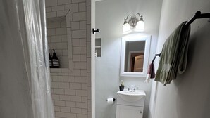 A bathroom with a white sink, a mirror, a towel rack, and a shower area. - Jungle House Studio Suites – Short North & Convention Center (Columbus)