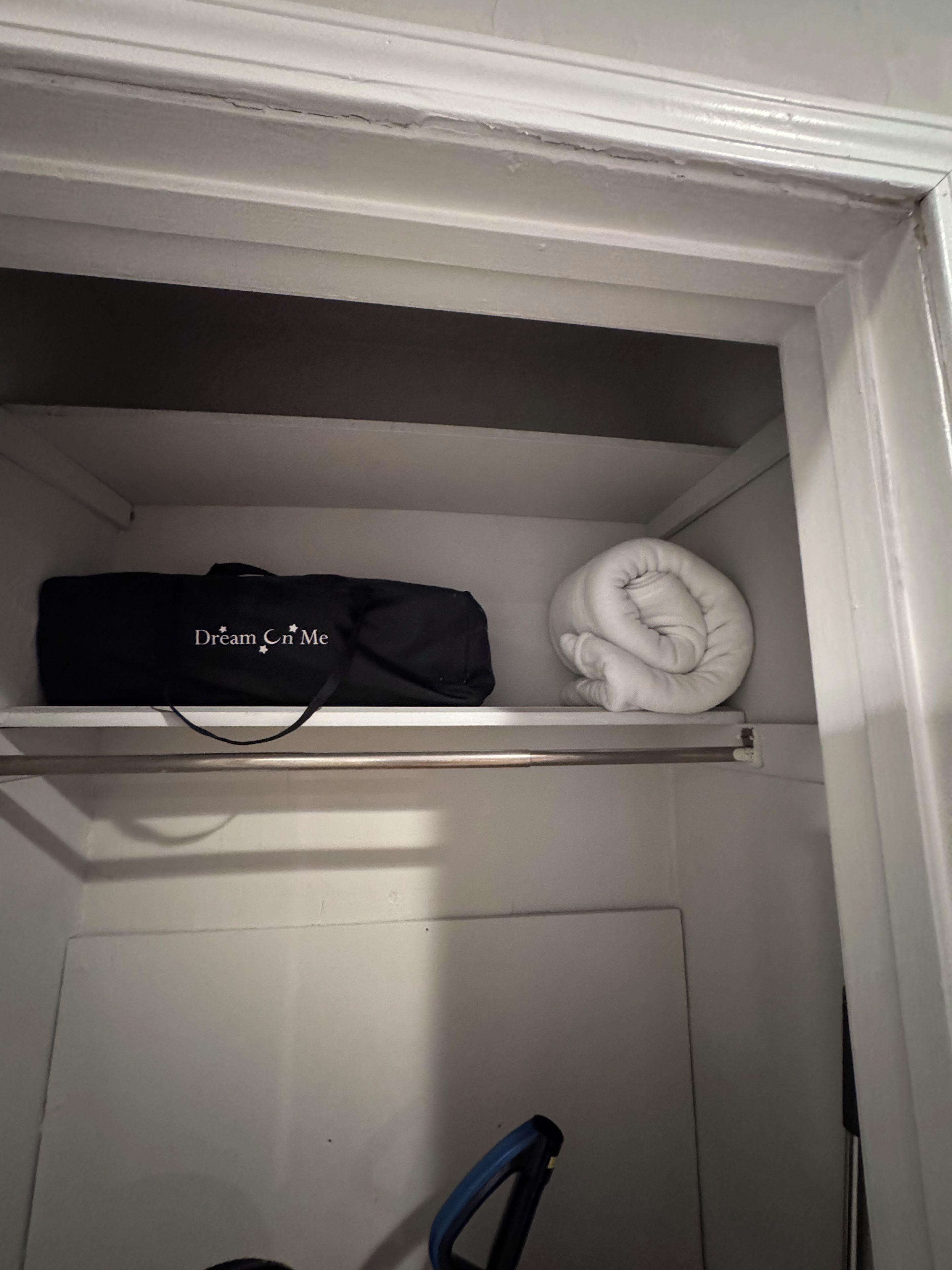 Un placard avec une étagère contenant un sac noir et un vêtement blanc plié.