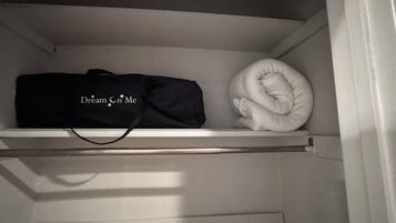 Un placard avec une étagère contenant un sac noir et un vêtement blanc plié.