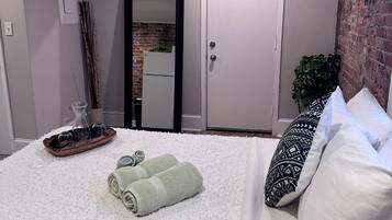 Quarto com cama, travesseiros, mesa de cabeceira e um copo sobre ela, e uma porta.