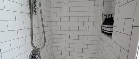 Een douche met witte betegelde wanden, een douchekop, een handdouche en een klein plankje met flessen.