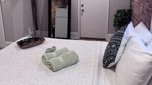 Ein Schlafzimmer mit einem Bett, Kissen, einem Nachttisch mit einem Glasflaschenkrug und einer Tür.