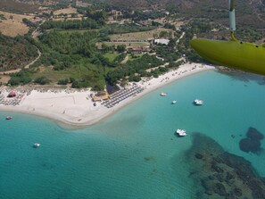 Vista aérea de uma área costeira com praia, barcos e um grande complexo de edifícios.