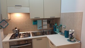 Een kleine keuken met een gasfornuis, spoelbak en witte kastjes.