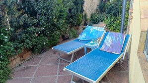Two sun loungers with blue cushions, a small table with a bowl of snacks, and a garden with various plants and flowers. - Casa Iride - a breath away from the sea
A stone's throw from paradise (Chia)