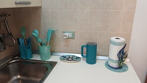 Een keuken met een spoelbak, een teal bestekhouder, een bord, een mok en een rol keukenpapier.