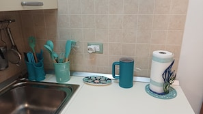 Uma cozinha com uma pia, um porta-utensílios verde-água, um prato, uma caneca e um rolo de papel toalha.