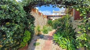 A garden pathway leading to a house with a stone wall, various plants, and a clear blue sky. - Casa Iride - a breath away from the sea
A stone's throw from paradise (Chia)