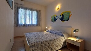 A bedroom with a bed, a nightstand, a lamp, a wall-mounted light, and a window with curtains. - Casa Iride - a breath away from the sea
A stone's throw from paradise (Chia)