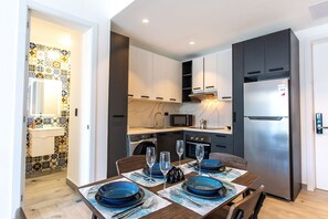 A modern kitchen with a built-in microwave, stove, and refrigerator. There is a dining table set with blue plates and wine glasses. - Modern 1BR, pools, gym, and artificial beach (Punta Cana)