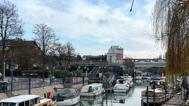 A canal with boats docked, a bridge in the background, and buildings along the water. - Comfortable Studio for 2 by the Marne (Nogent-sur-Marne)