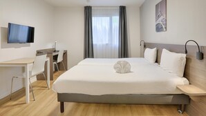 A hotel room with a bed, a desk, a chair, a flat-screen TV, and a window with curtains. - Comfortable Studio for 2 by the Marne (Nogent-sur-Marne)