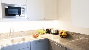 Una cucina con forno a microonde integrato, lavello, piano di lavoro con tagliere, bollitore e una ciotola di frutta.