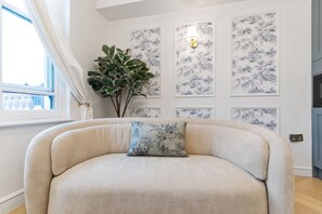 Ett rum med en stor, böjd soffa, en krukväxt och flera inramade konstverk på väggen.