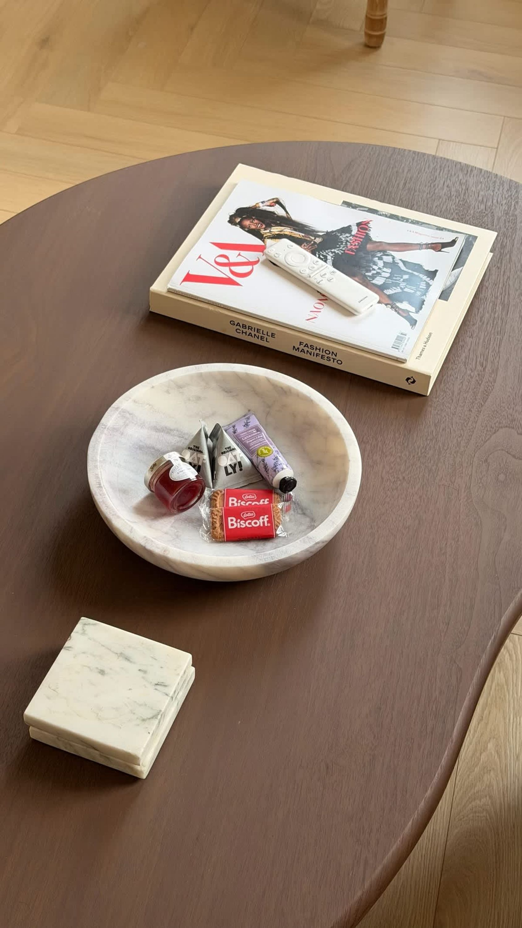A round table with a magazine, a remote control, a bowl with snacks, and a small box.