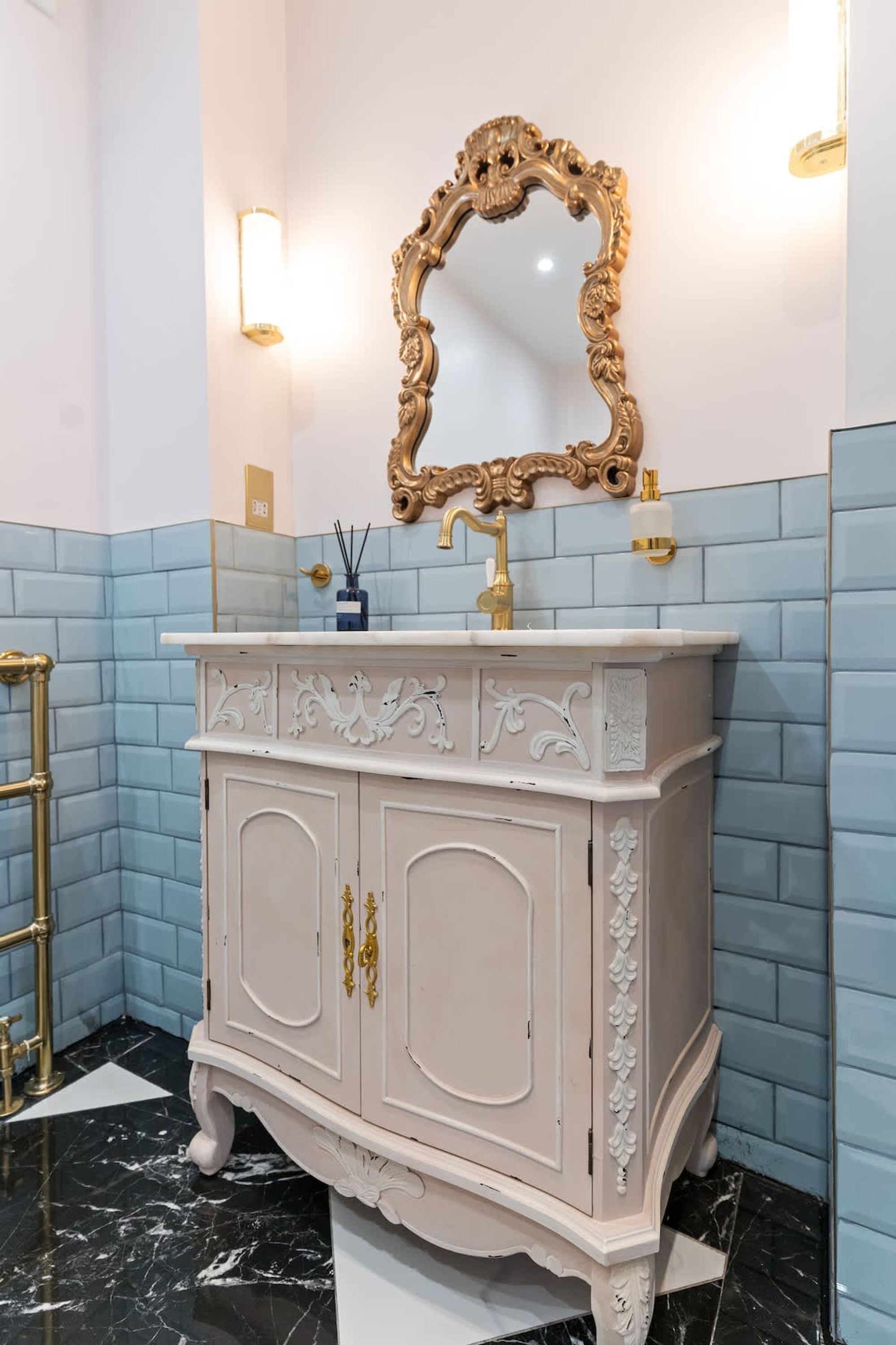 A bathroom with a white vanity, gold faucets, a gold-framed mirror, and blue-tiled walls.