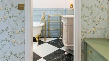 A bathroom with floral wallpaper, a black and white checkered floor, a white bathtub, and a green cabinet.