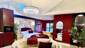 A modern hotel room with a bed, a sofa, a chandelier, a TV, and a bathroom visible through an archway. - Boutique Studio Gold Bath in Jewellery Quarter BHM (Birmingham)