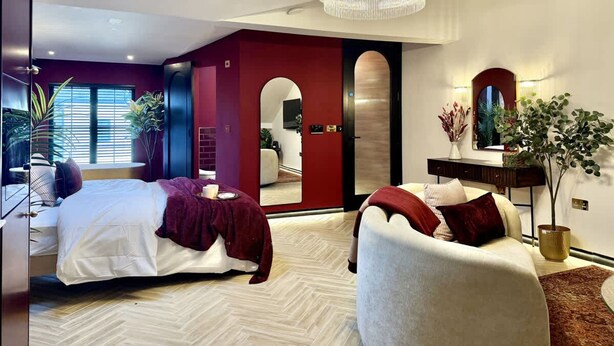 A modern bedroom with a bed, a sitting area, a chandelier, and a large mirror. - Boutique Studio Gold Bath in Jewellery Quarter BHM (Birmingham)