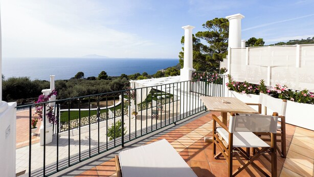 Eine Terrasse mit Blick auf das Meer, weißen Säulen und einem Tisch mit Stühlen.