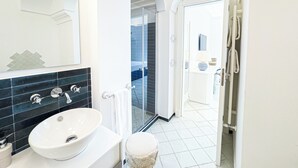 Ein modernes Badezimmer mit einem weißen Waschbecken, schwarzen Fliesen, einem Spiegel und einer Duschkabine aus Glas.
