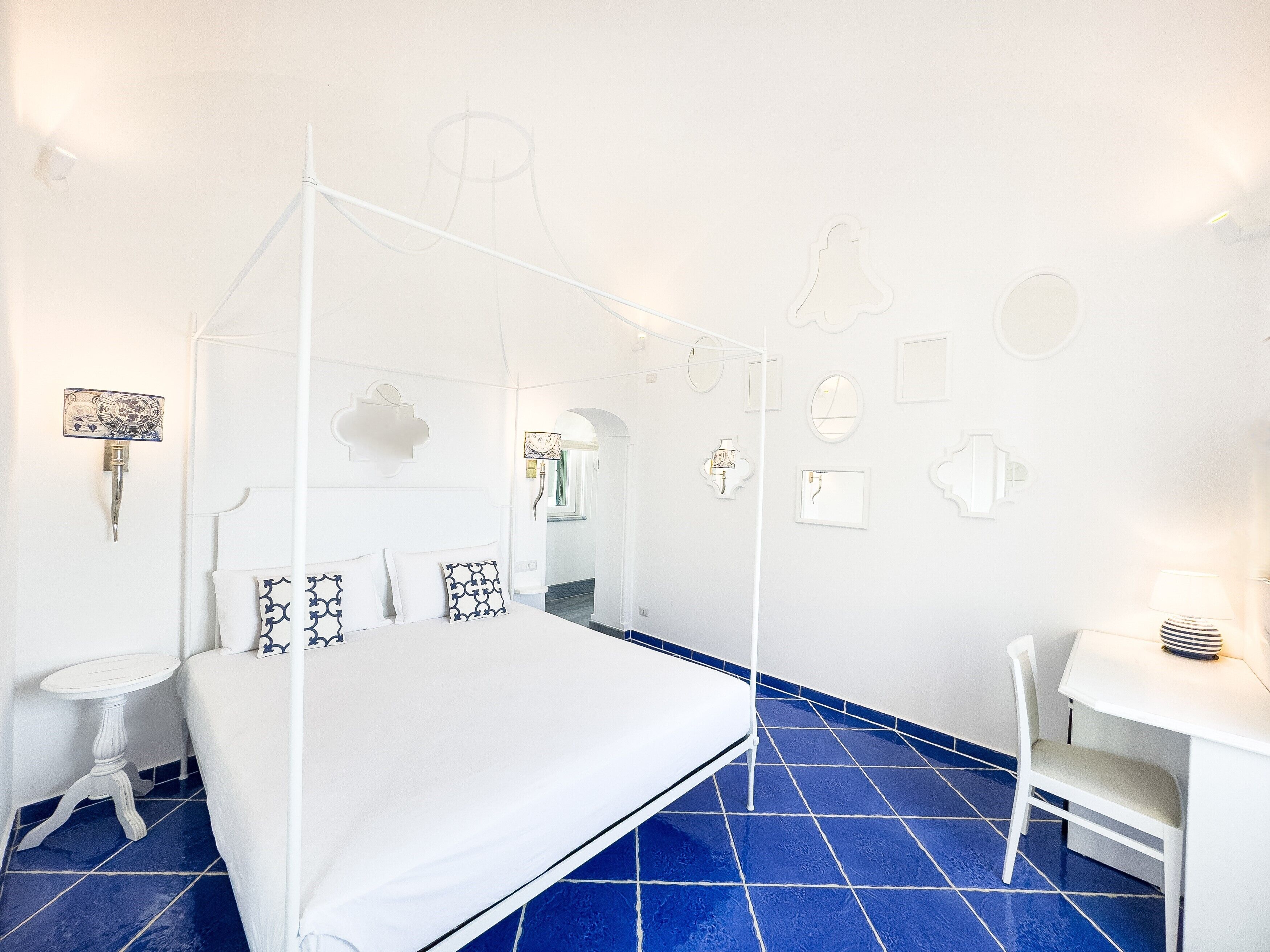 Quarto com cama de dossel, mesinha de cabeceira, uma cadeira e escrivaninha com abajur.