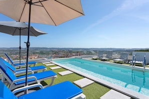 Ein Pool auf dem Dach mit blauen Liegestühlen und Blick auf die Stadt.