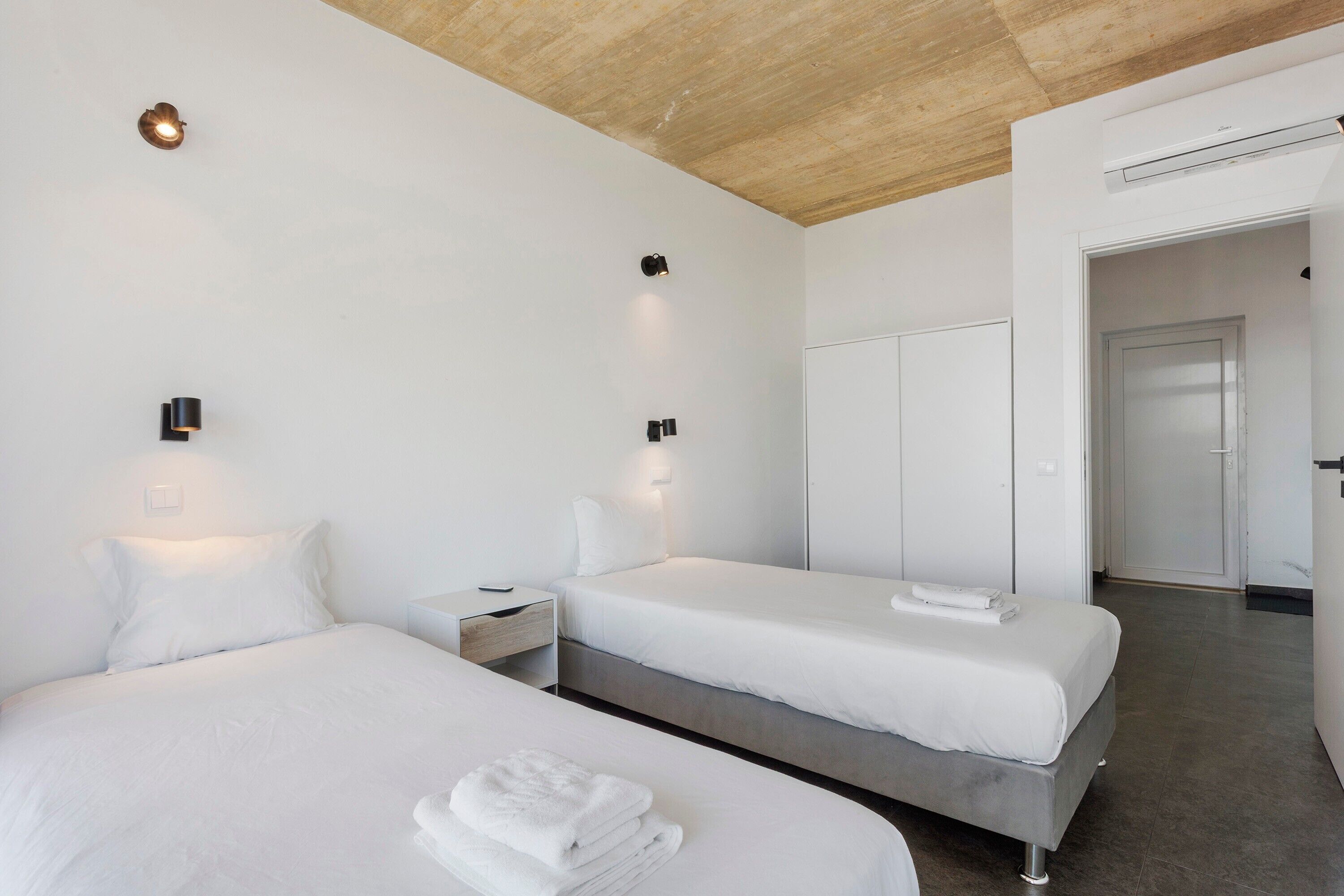 A modern hotel room with two beds, a wooden ceiling, and a wardrobe.