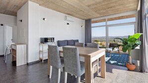 A modern living room with a wooden dining table, grey upholstered chairs, a sofa, and a large window with a view. - Apartment 'Colina Do Sol 1' with Mountain View, Wi-Fi and Air Conditioning (Vau)