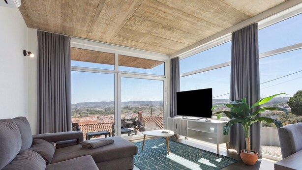 A modern living room with a sofa, a TV, a potted plant, and a view of the city. - Apartment 'Colina Do Sol 1' with Mountain View, Wi-Fi and Air Conditioning (Vau)
