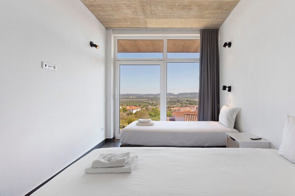 A hotel room with a large window, a bed, a bedside table, and a nightstand.