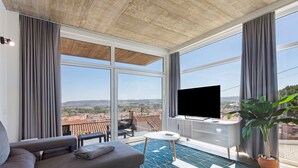 A modern living room with a sofa, a small table, a TV, and a balcony with a view of the city. - Apartment 'Colina Do Sol 1' with Mountain View, Wi-Fi and Air Conditioning (Vau)