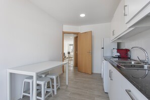 Una cocina compacta con encimera blanca, un lavabo y una cafetera roja.