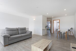 Una sala moderna con un sofá gris, una mesa de centro de madera y un comedor con una mesa y sillas blancas.