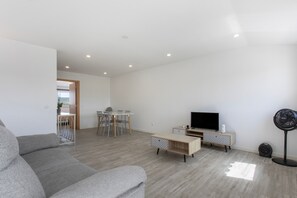 Uma sala de estar moderna com um sofá cinzento, uma televisão, uma mesinha e um ventilador.