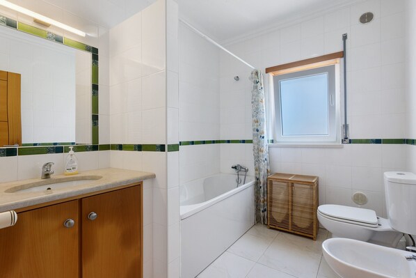 A bathroom with a bathtub, toilet, sink, and a window.