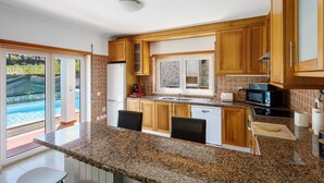 A kitchen with granite countertops, wooden cabinets, a dishwasher, a microwave, and a window overlooking a pool.