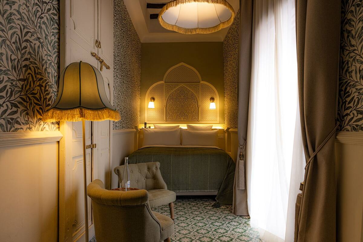 A room with a bed, a chair, a lamp, and a patterned wall.