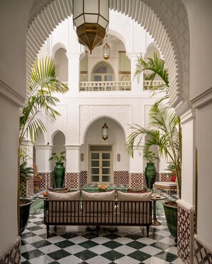 Un patio interior con suelo a cuadros, un banco central y arcos.