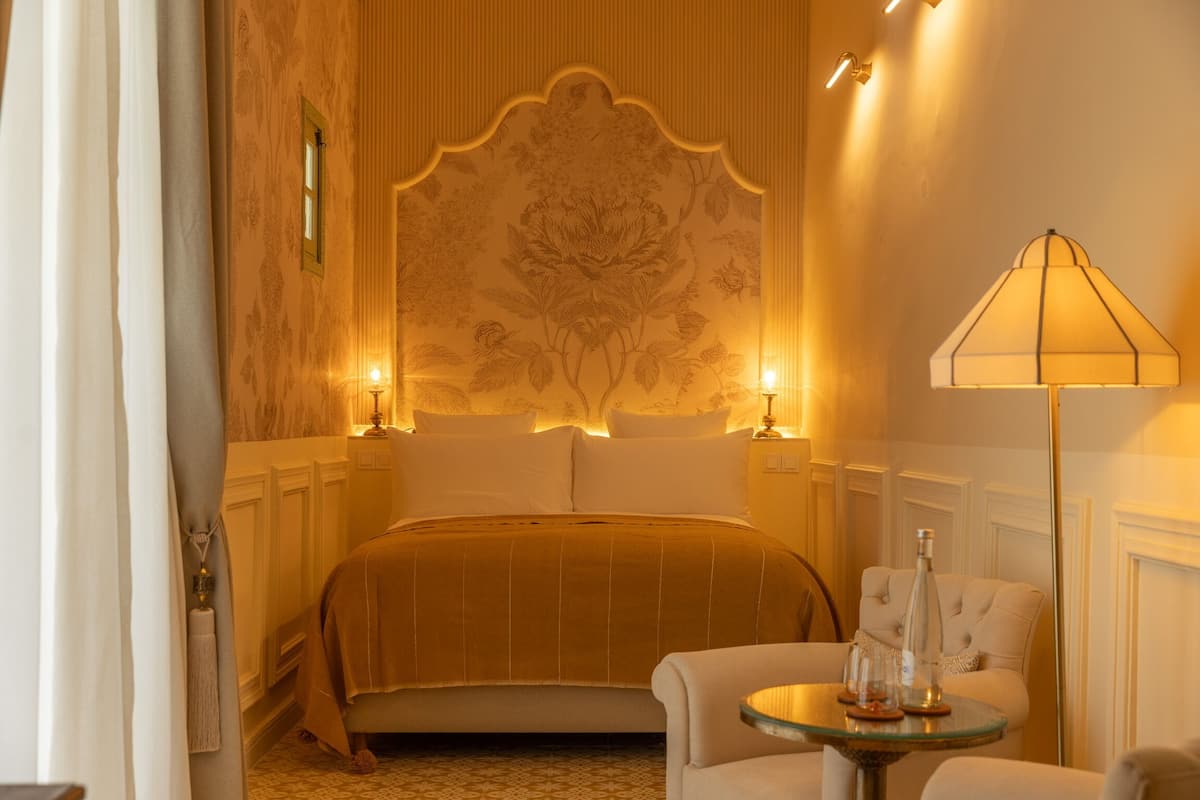 A hotel room with a bed, a round table with a lamp, and a chair.