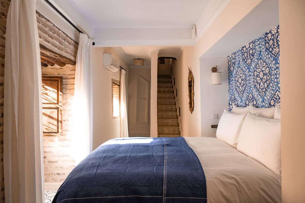A bedroom with a bed, a staircase, a wall with a decorative pattern, and a door leading to another room.