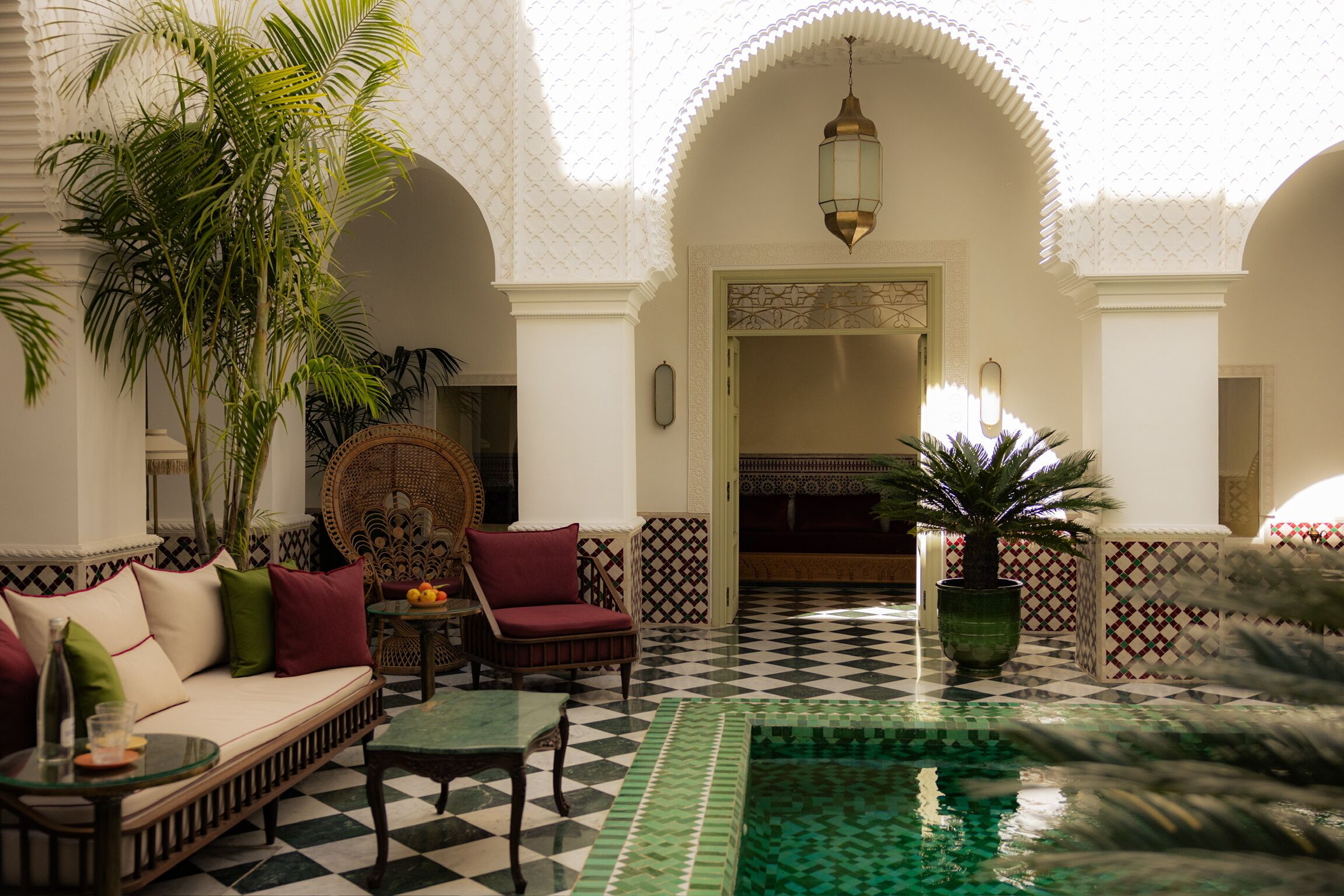 A courtyard with a checkered floor, a pool, seating area, and a doorway leading to another room.