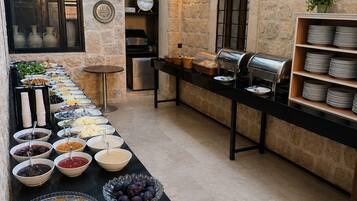 Montaje de bufé con diversas opciones de comida, un reloj y una estación de café en una sala de paredes de piedra con techo de vidrio.