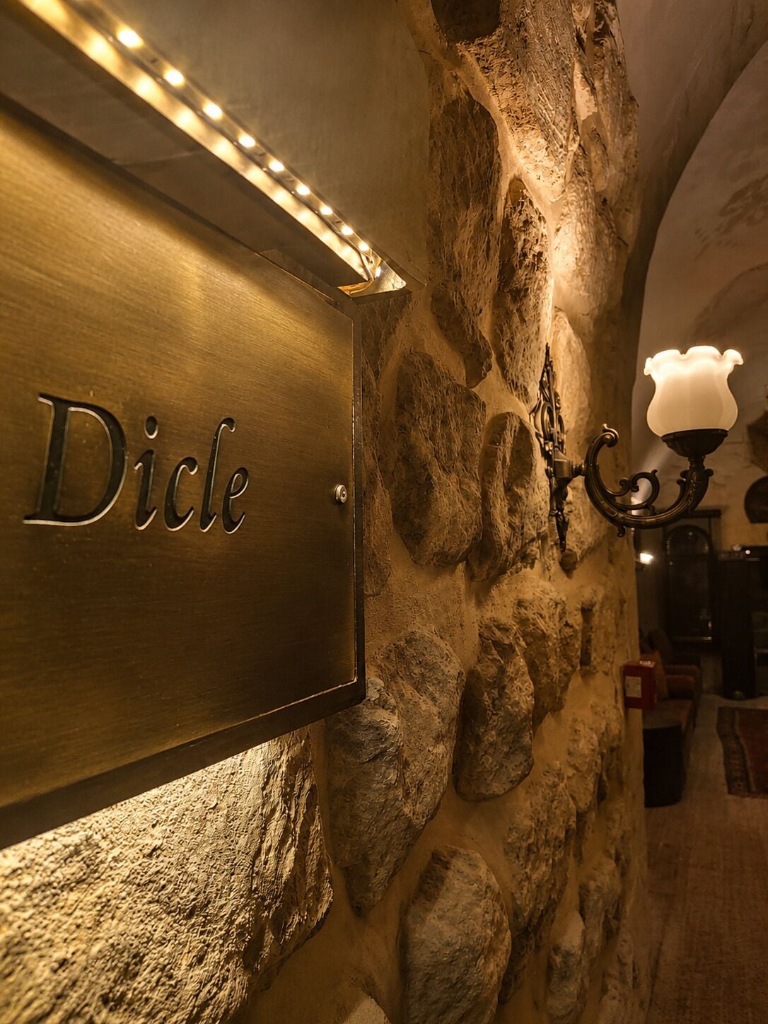 A stone wall with a sign reading 'Dicle' and a wall-mounted lamp.
