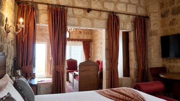 A stone-walled room with a bed, red curtains, a wooden dresser, and a television.