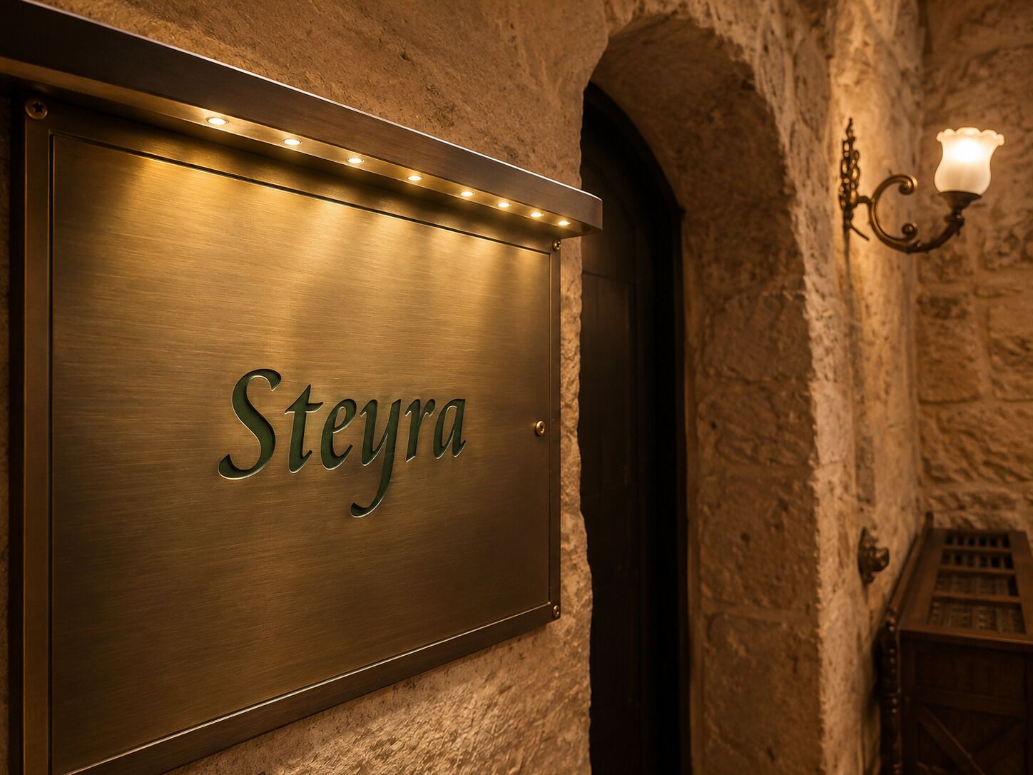 A metal sign with the name 'Steyra' mounted on a wall with stone architecture.