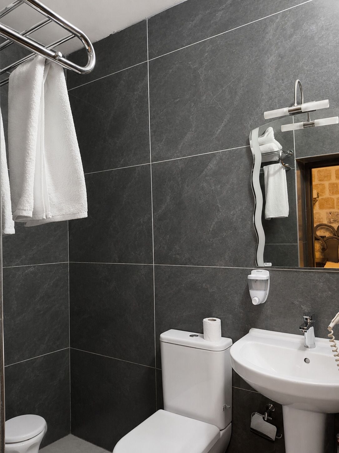 A bathroom with dark tiles, a white toilet, a sink, and a towel rack.