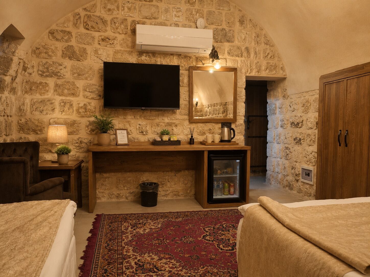 Une pièce chaleureuse avec un mur en pierre, un téléviseur à écran plat, un petit réfrigérateur, un meuble en bois et un tapis rouge à motifs.